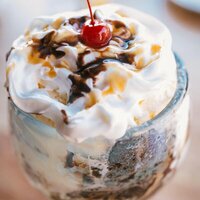 ice cream in a glass cup with toffee sauce drizzled on top decorated with a cherry