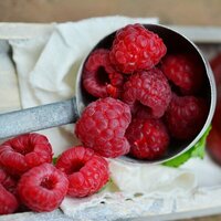 a metal spoon with whole raspberries spilling, raspberry, bright red pink violet