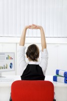 Rear view of young businesswoman sitting at desk stretching. Copy space