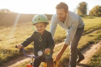 Photo of a young boy who is learning to ride a bicycle with a little help from his father
