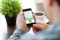 man holding a phone with social network on the screen at a table in a cafe