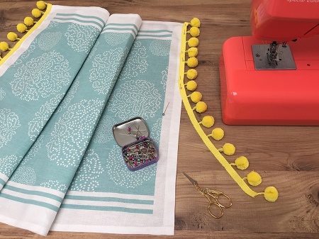 pinning pompom braid onto an asha tea towel