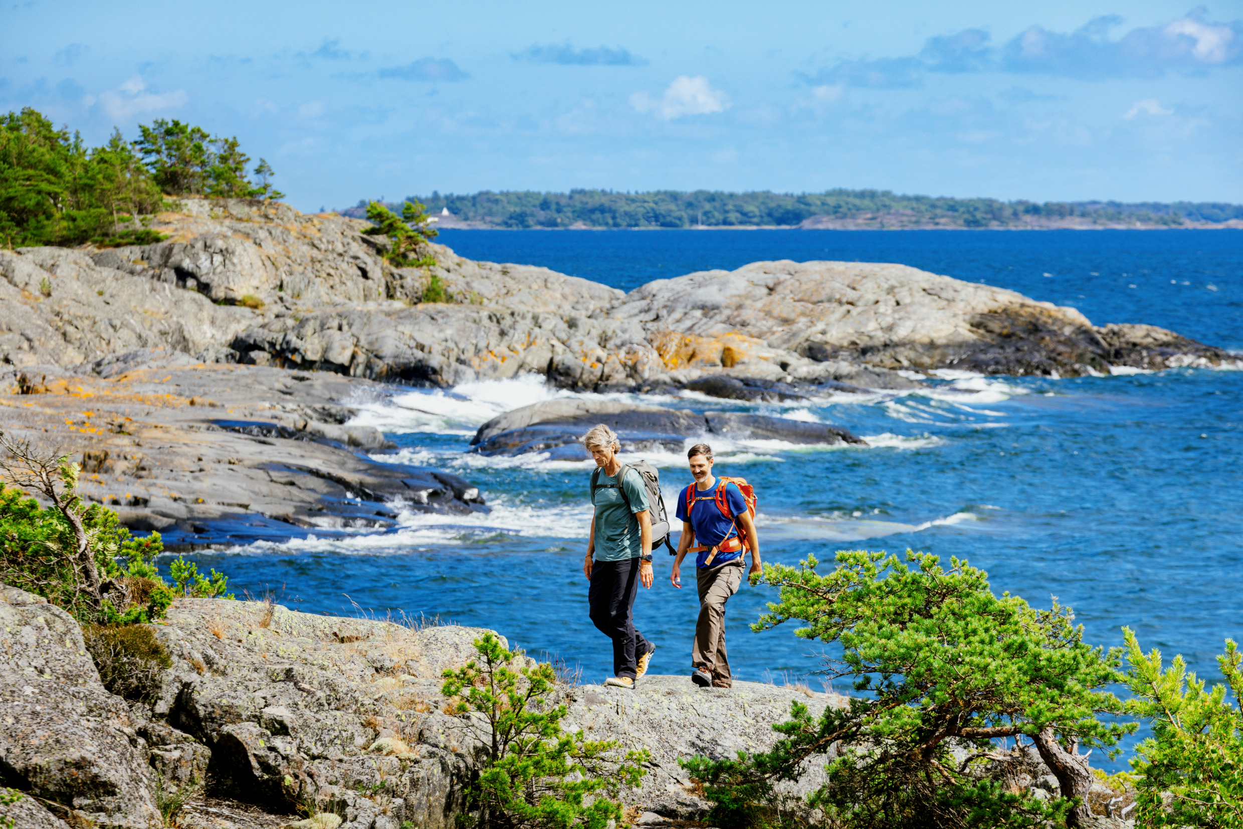 Two men are walking on cliffs by the sea on a sunny summer day.
