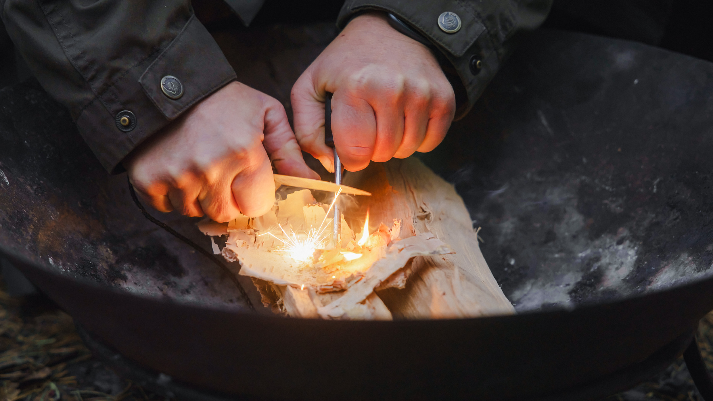En person tänder en eld för att laga mat på en eldplats i skogen.