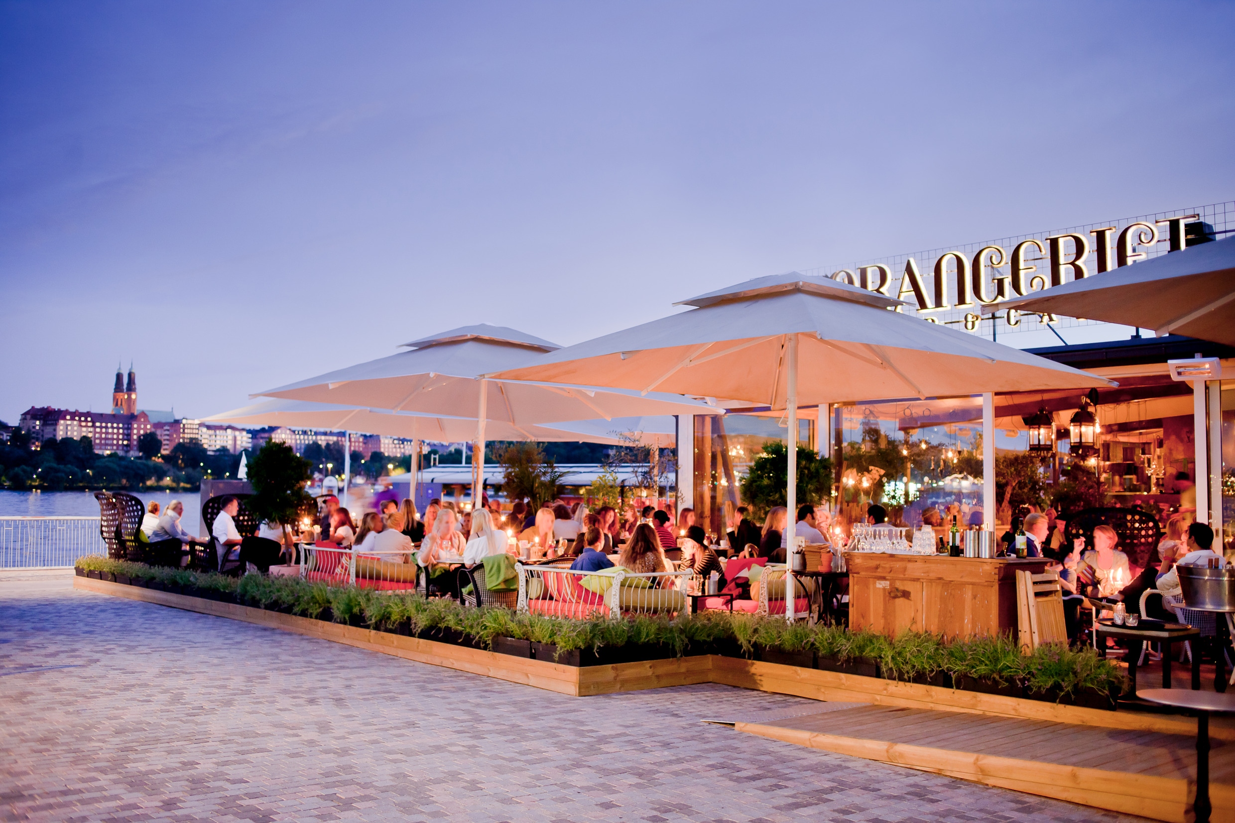 En utomhusrestaurang i Stockholm en ljus sommarnatt. Restaurangen är fylld av människor som sitter och äter och dricker gott.
