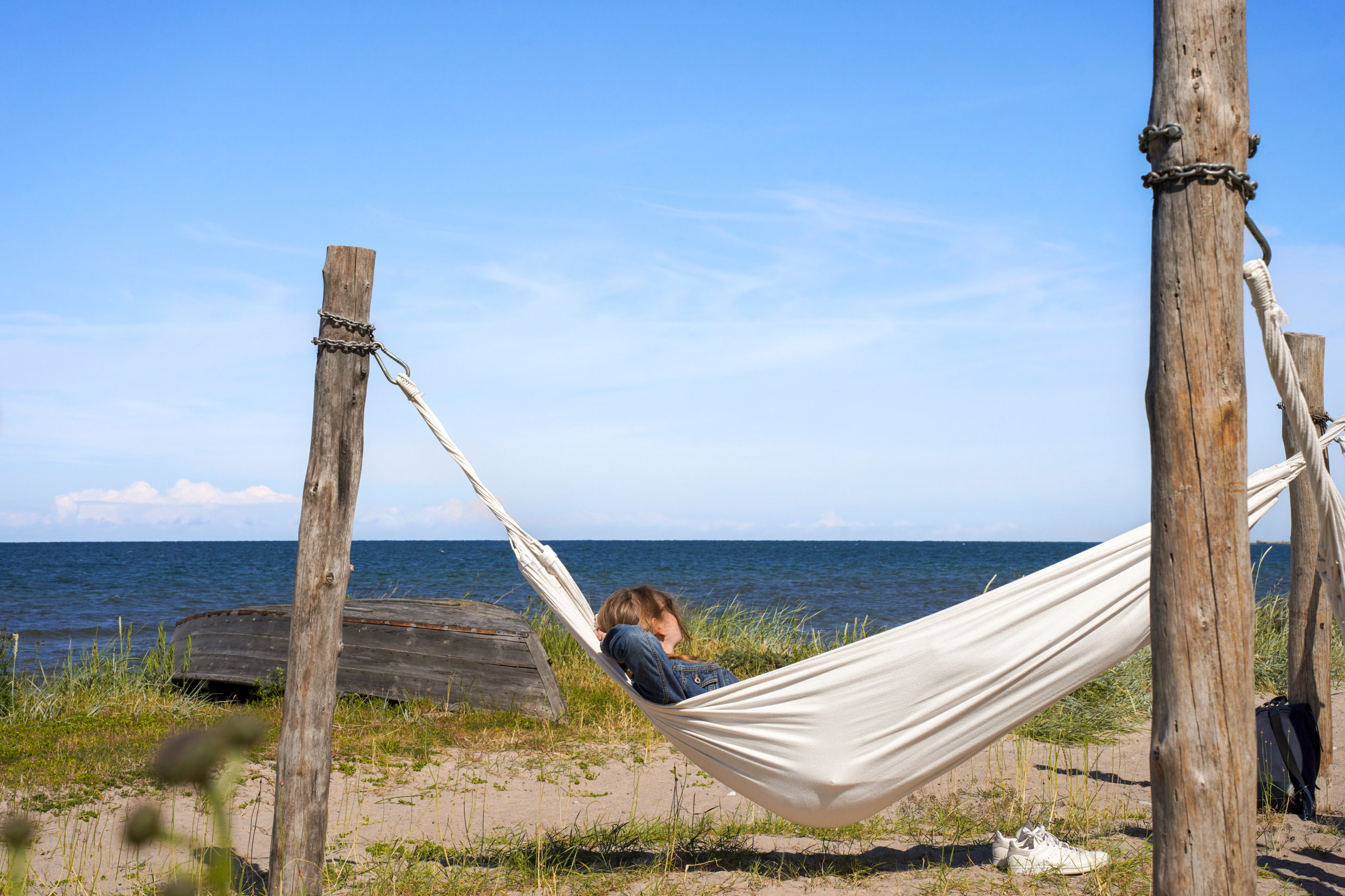 En person ligger i en hängmatta och tittar ut över havet.
