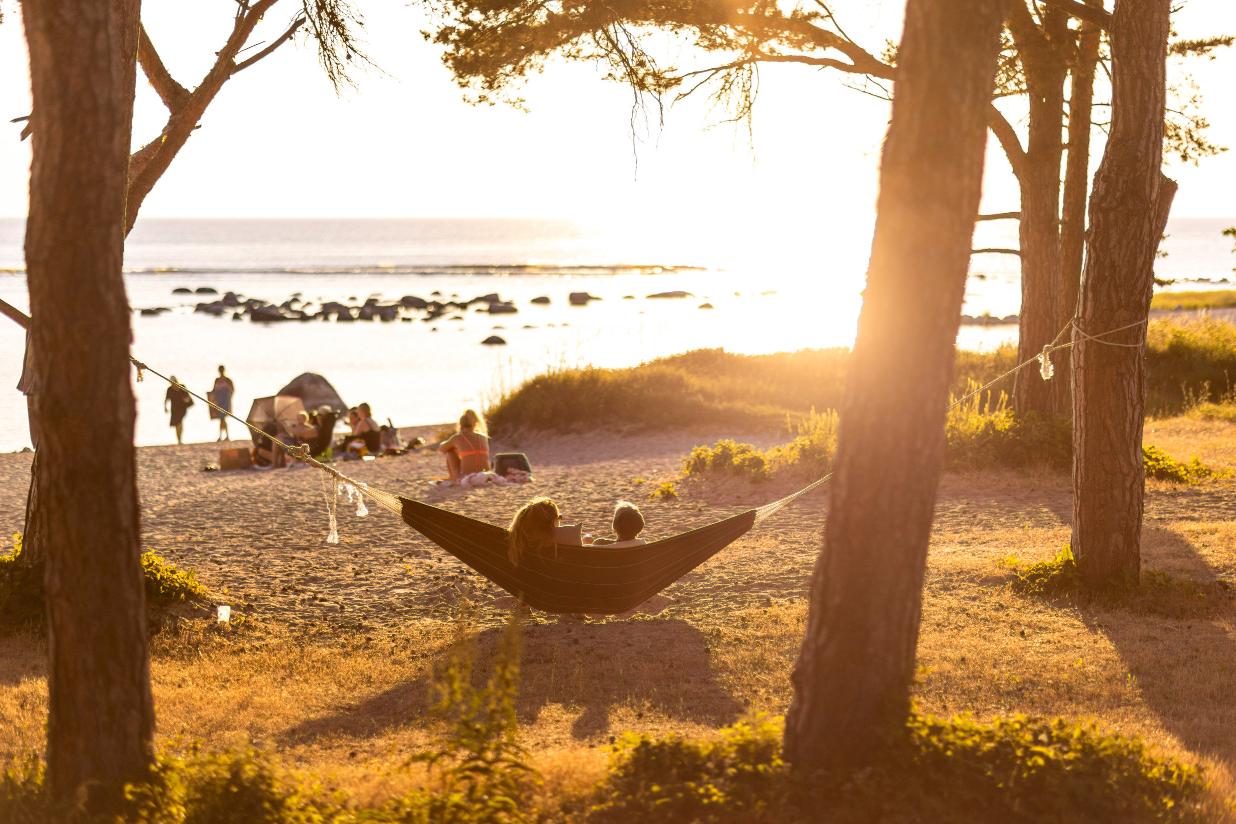 Två personer hänger i en hängmatta på stranden i solnedgången.