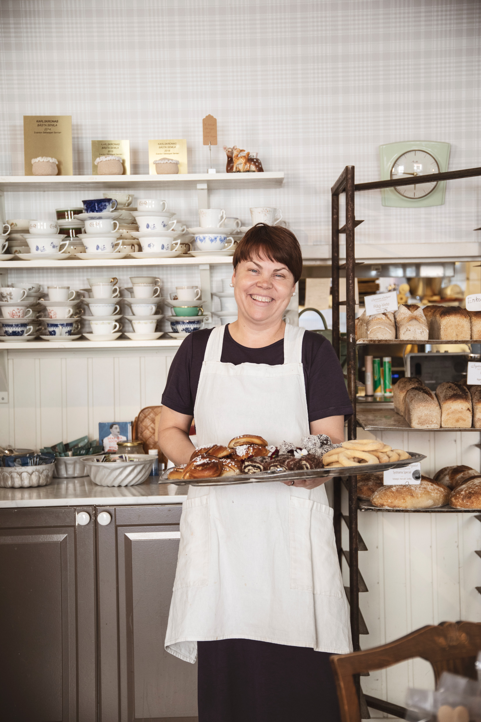 En konditor står med en hel plåt full med bullar i ett konditori.